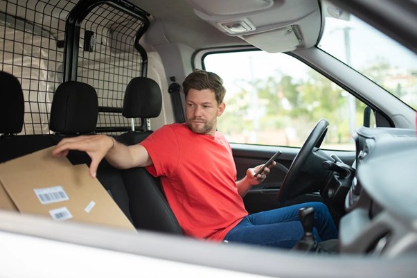 man sitting in a van holding a phone about to deliver a parcel.